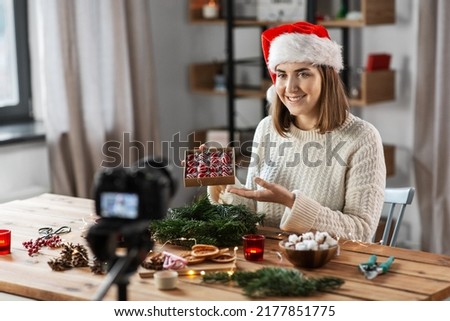 winter holidays, diy and video blogging concept - happy smiling woman or blogger in santa hat with camera and box of christmas balls making fir wreath at home