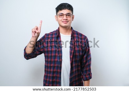 Young handsome Asian man wearing casual clothes showing and pointing up with fingers number one while smiling confident and happy isolated over white background Royalty-Free Stock Photo #2177852503