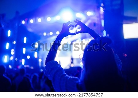 Heart shaped hands at concert, loving the artist and the festival. Music concert with lights and silhouette of people enjoying the concert. Royalty-Free Stock Photo #2177854757