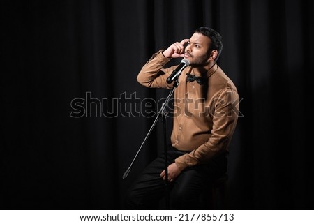 thoughtful indian comedian performing stand up comedy and telling jokes in microphone on black