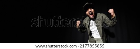 emotional and stylish indian hip hop singer in cap singing loud on black, banner