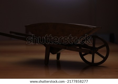 The silhouette of an old wheelbarrow carrying certain bulky things photographed on a brown surface