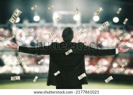 Rear view of soccer manager expressing happy while standing under falling money in the stadium