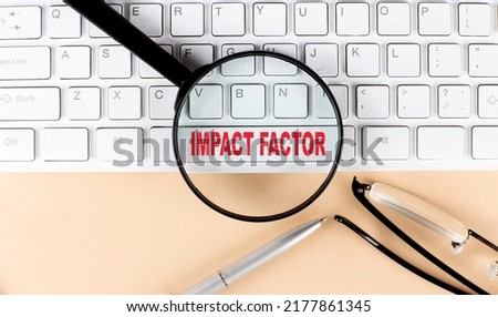 Text IMPACT FACTOR on keyboard with magnifier , glasses and pen on a beige background