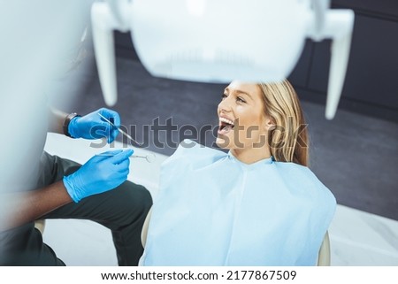 Amazing smile! Top view of dentist examining his beautiful patient in dentist’s office. Dentist examining teeth of her female patient during appointment at dental clinic. Focus is on young woman