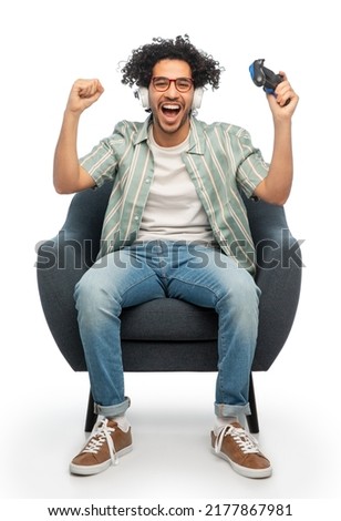 technology, people and leisure concept - happy smiling young man in headphones with gamepad playing video game and celebrating success, over white background