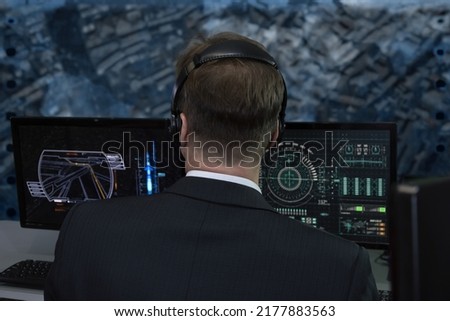 A secret agent wearing headphones watches monitors and monitors in a military intelligence center. Concept: human surveillance, government official, military intelligence officer.