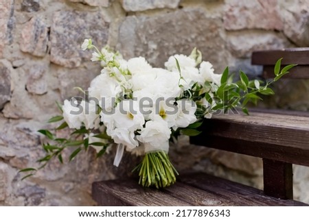 Wedding bouquet with white flowers on a wooden stairs near stone wall. Bouquet with peonies,lisianthus eustoma and ruscus Royalty-Free Stock Photo #2177896343