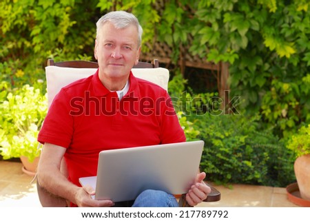 Portrait of senior man sitting at nursing home garden and using his laptop.