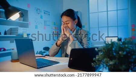Young Asia businesswoman sit with laptop and tablet on desk rubbing eye feel pain and tired from overwork in office at night. Female suffer of office syndrome long work, Mental Health workplace. Royalty-Free Stock Photo #2177899947