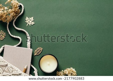 Flat lay aesthetic feminine workspace with macrame handbag, candle, dried flowers on green background. Top view cozy home, bohemian woman office desk table. Autumn, fall concept. Royalty-Free Stock Photo #2177902883