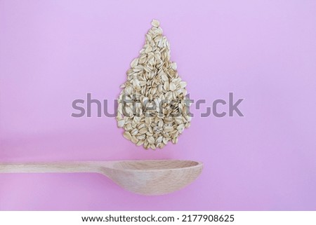 Oatmeal in wood spoon on pink background, rolled oats