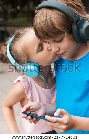 Attractive little girl kisses a boy on the cheek. Children hold phones in their hands. Students play video games and listen to music
