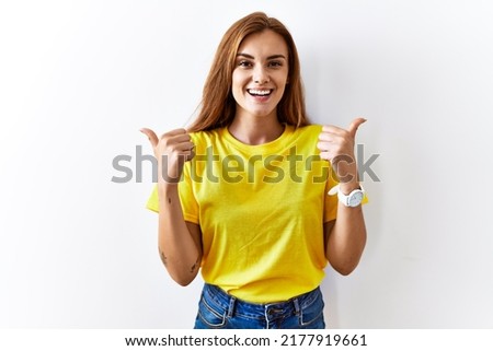 Young brunette woman standing over isolated background success sign doing positive gesture with hand, thumbs up smiling and happy. cheerful expression and winner gesture. 