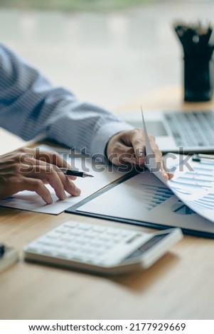 Businessman hand holding a pen to work with charts, graphs and analyze business strategies. financial statistics with laptop sit at desk vertical view