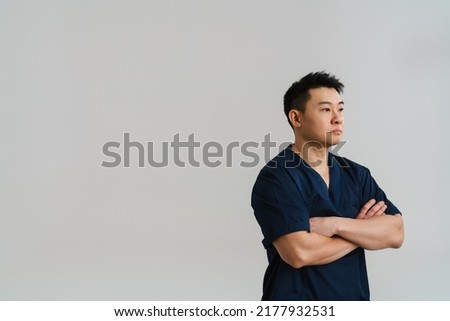 Adult asian man wearing medical uniform posing at camera standing isolated over white background