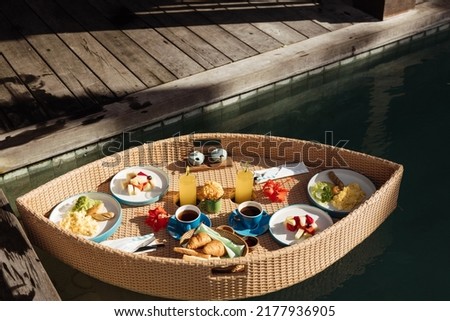 Breakfast in swimming pool, floating breakfast set in tray in resort. Set of floating breakfast tray in swimming pool with fried egg omelette, fruit, juices, sausage, ham, bread and other.