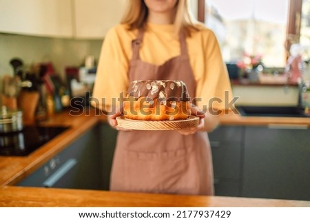 Smiling young blonde woman chef cook in apron standing at the kitchen, showing tasty pie.  Royalty-Free Stock Photo #2177937429