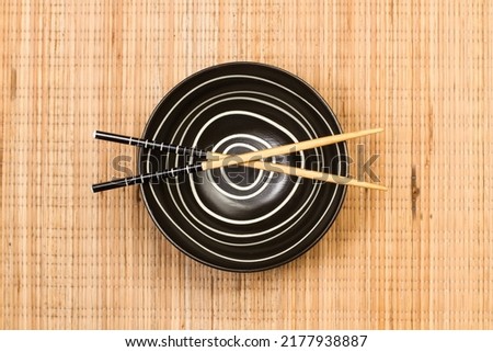 Chopsticks on a black bowl and on a bamboo table mat in a top view