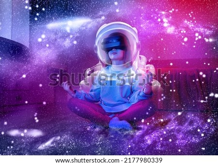 Child girl wearing virtual reality headset like as astronaut and looking at digital space system. Space exploration with augmented reality glasses. Kid is sitting on flor at childroom. Royalty-Free Stock Photo #2177980339