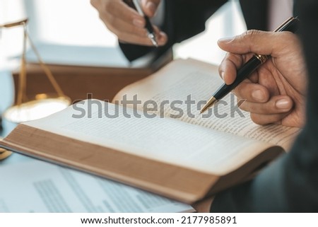 Two lawyers are reading a large book of law to jointly draft a prosecution contract and look at the details of the case for defending their clients. The concept of law and justice.