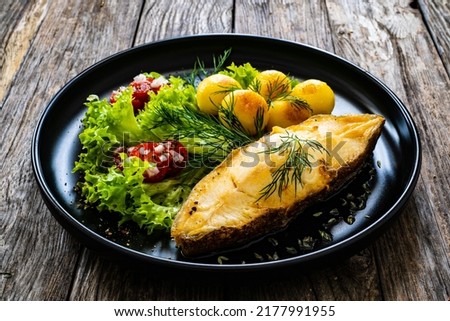 Fish dish - fried halibut with fried potatoes, cherry tomatoes and leafy greens on wooden table 