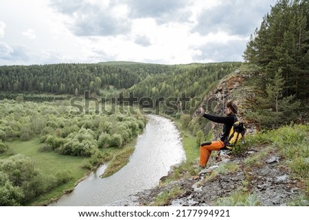 A man sits on a rock in the mountains, a selfie on his phone, a guy shoots a video on a trip on a smartphone, a beautiful panorama in the mountains, a tourist shooting of himself. High quality photo