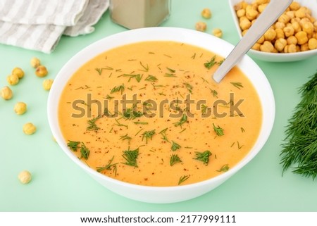 Chickpea cream soup in white bowl with spoon on green background. Healthy vegetarian lean dinner or lunch.