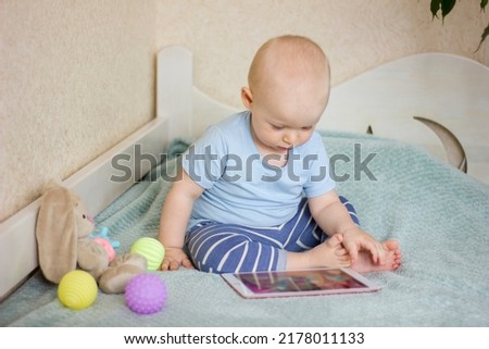 Cute toddler baby boy sitting on the bed at home, using digital tablet and watching cartoons. Child is using modern technology. Focus picked.