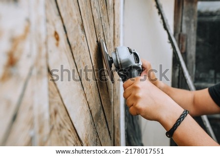 Closeup photo of a professional male worker who is sanding a wooden door using an electric grinder.