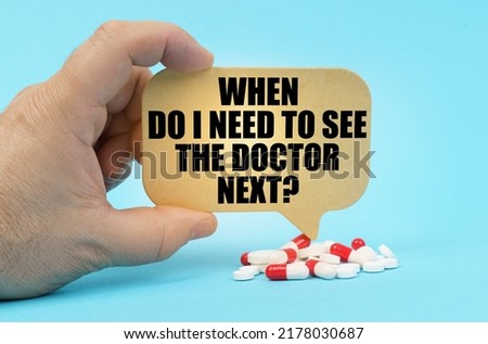 Medical concept. On a blue surface are pills in a persons hand, a sign with the inscription - When do I need to see the doctor next
