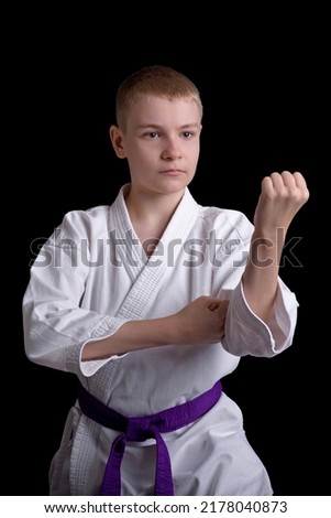 Teen boy in a white kimono with a blue belt demonstrates a karate blocking gesture, wkf, karate kid