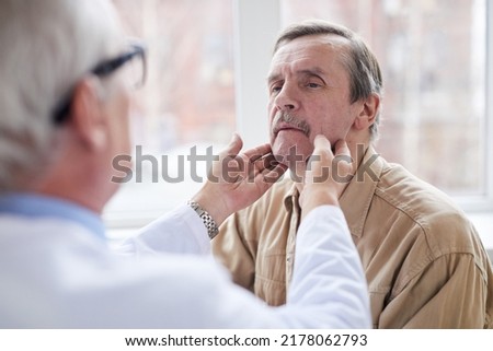 Over shoulder view of doctor checking lumps on neck of aged male patient with mustache at appointment