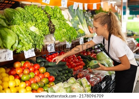 Teenage girl in uniform working in grocery shop as first job experience, selling cucumber Royalty-Free Stock Photo #2178096709