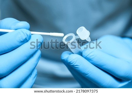 Doctor holds a COVID-19 swab collection, wears blue gloves and a PPE protective  and carries a test tube to collect the OP NP and test coronavirus. Royalty-Free Stock Photo #2178097375