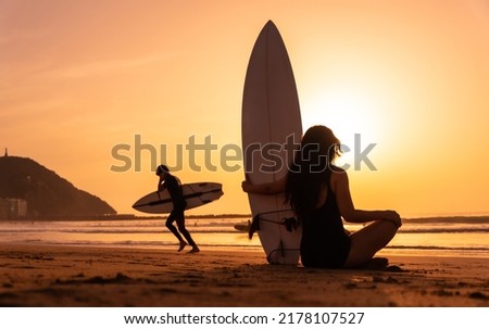 Silhouette of a surfer woman on a beach at sunset with the surfboard