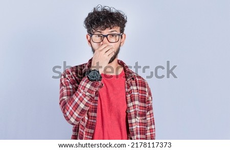 Person holding his nose looking at camera, people holding his nose with unpleasant smell expression, young man with bad smell expression holding his nose Royalty-Free Stock Photo #2178117373
