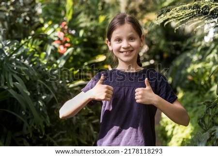 Happy girl with thumbs up on nature background. Portrait of beautiful Girl Smiling Teenager showing fingers up. Happy Children in Botanical Garden. Gardening and Landscaped