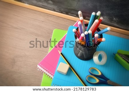 School supplies with pen with markers on notebooks with tools on wooden desk and blackboard. Elevated view. Horizontal composition. Royalty-Free Stock Photo #2178129783