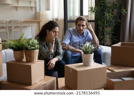 Unhappy young Caucasian man and woman sit on couch argue quarrel on moving day to new home. Distressed upset millennial couple renters have family misunderstanding relocating unpacking. Royalty-Free Stock Photo #2178136495