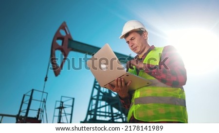 oil industry. engineer next to an oil rig. oil production business finance concept. gas production. a worker with a laptop monitors oil production next to an station. a worker in hard hat sun works