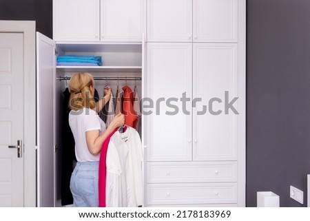A woman stands in front of a closet and chooses her clothes for a walk. Royalty-Free Stock Photo #2178183969
