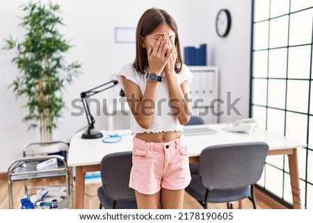 Young hispanic girl standing at pediatrician clinic rubbing eyes for fatigue and headache, sleepy and tired expression. vision problem 