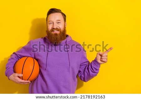 Photo of cute sweet man wear violet sweatshirt holding ball pointing empty space isolated yellow color background