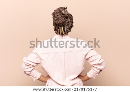 young woman feeling confused or full or doubts and questions, wondering, with hands on hips, rear view
