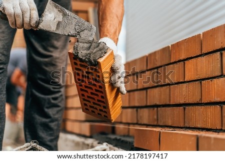 Mason trowels smears cement mortar on brick. Bricklaying when building house or stone fence Royalty-Free Stock Photo #2178197417