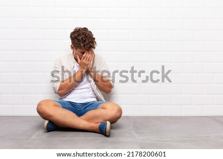 young man covering eyes with hands with a sad, frustrated look of despair, crying, side view