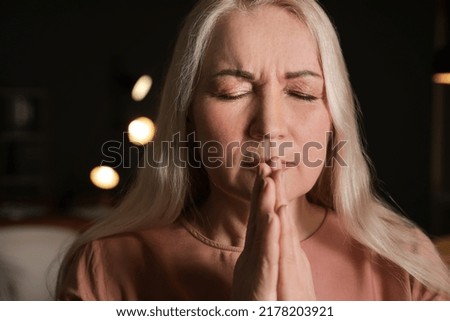 Religious mature woman praying in dark room