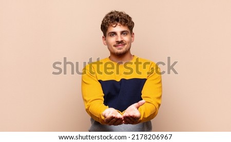 young man smiling happily with friendly, confident, positive look, offering and showing an object or concept