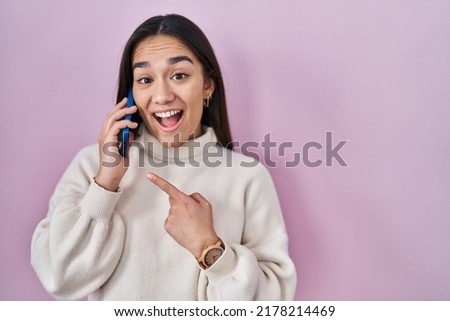 Young south asian woman having conversation talking on the smartphone smiling happy pointing with hand and finger 